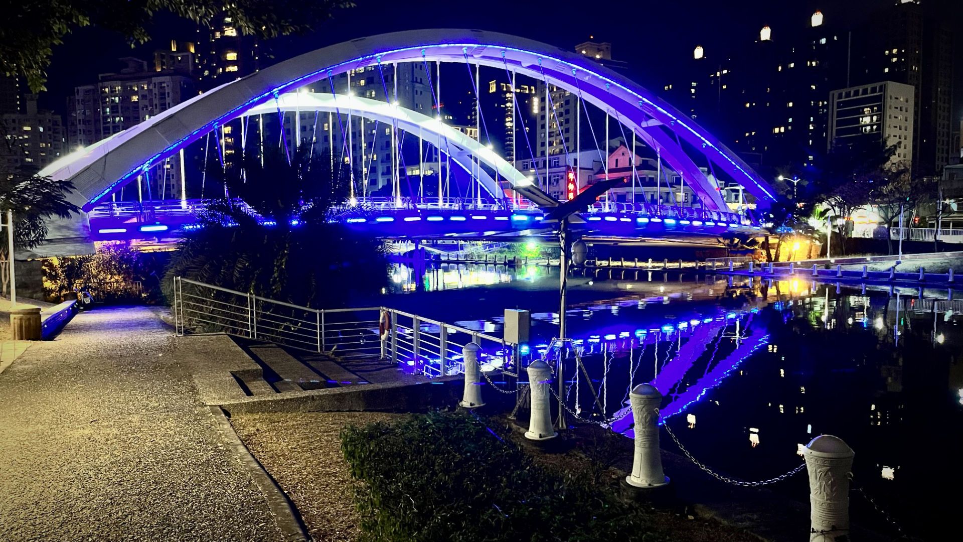 An arched road bridge across the river, illuminated in neon blue.