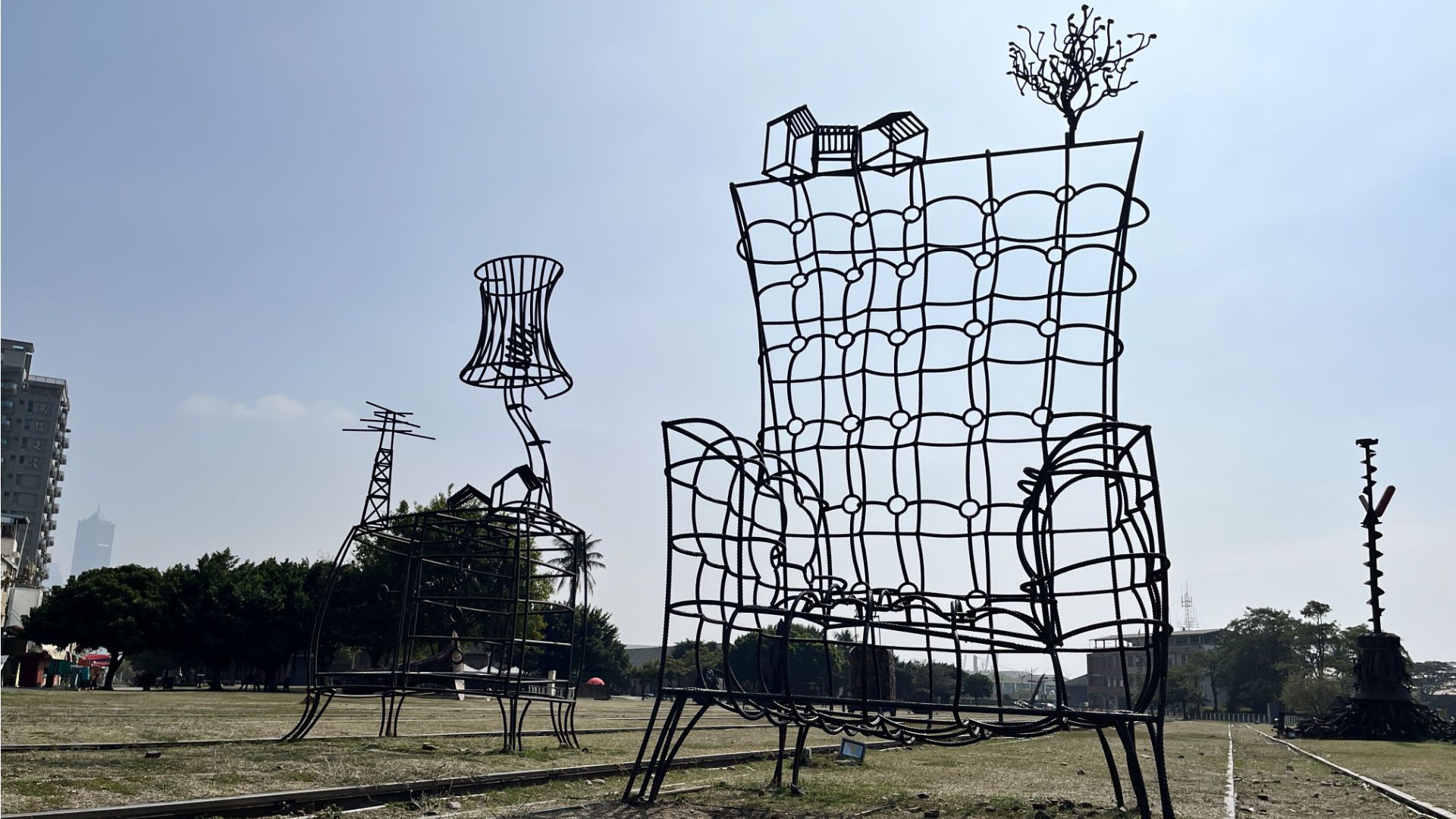 Wireframe sculpture of a giant armchair and sidetable with lamp on top.