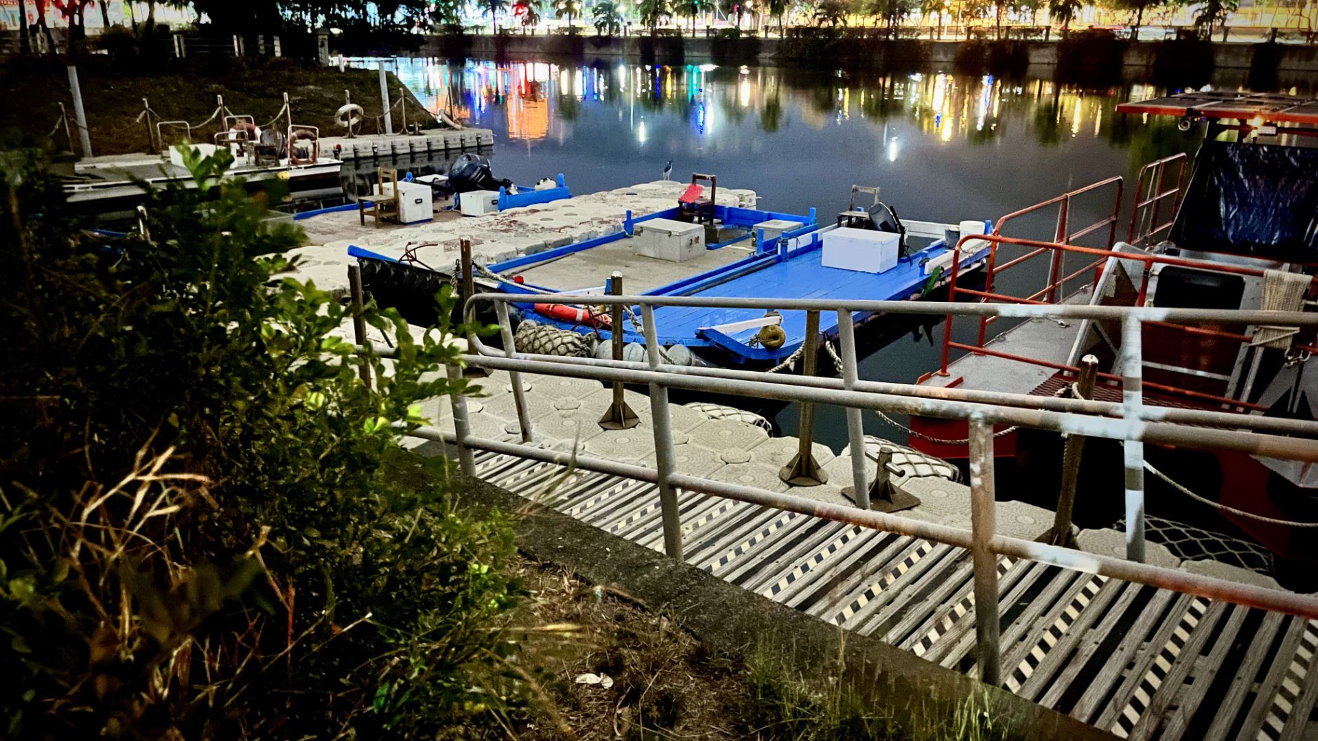 Four small boats docked on the edge of Love River. Three of the boats are flat, almost like barges, and one has a canopy over the deck.