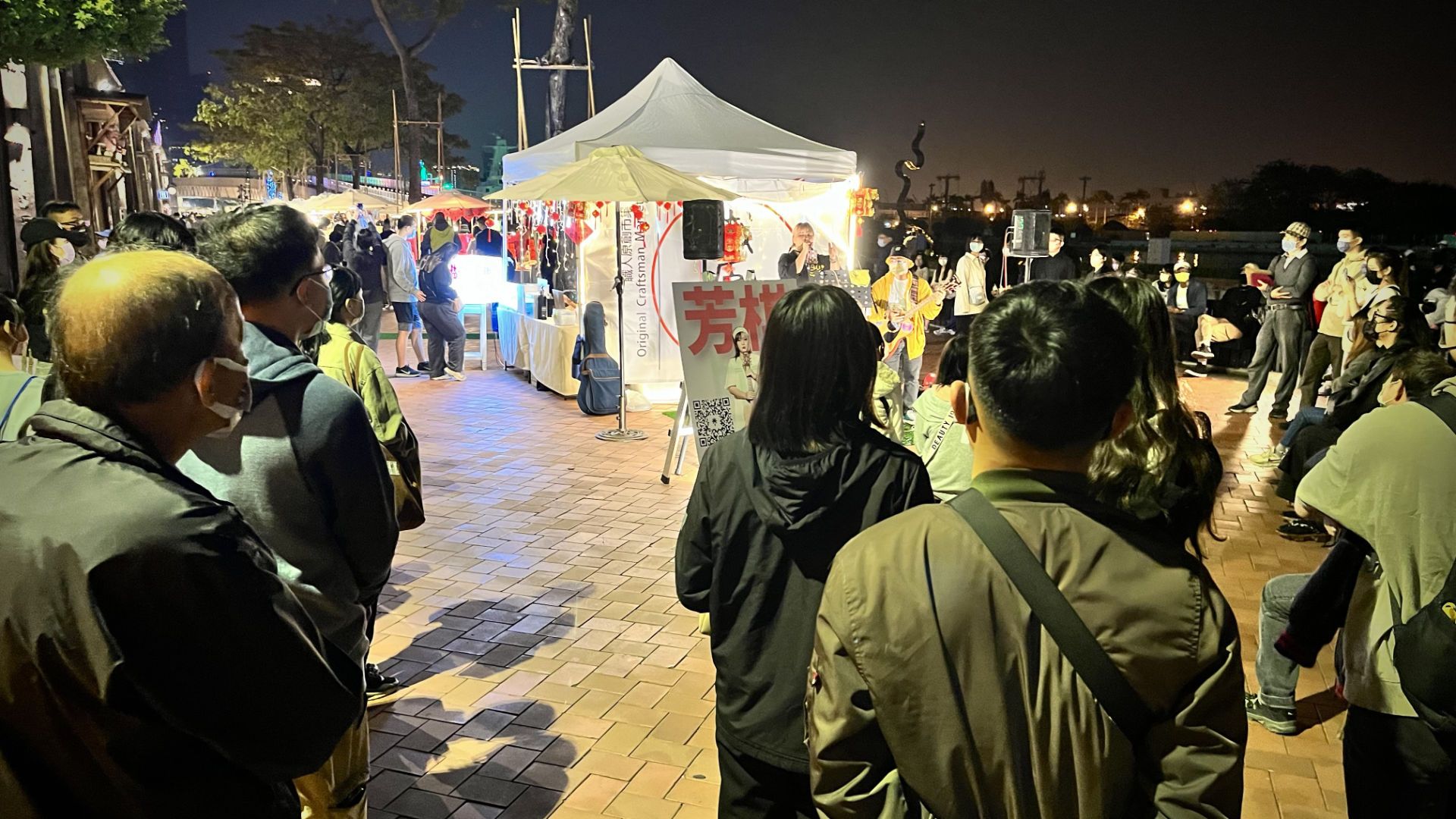 Two buskers singing to a crowd, under lights, at the market.