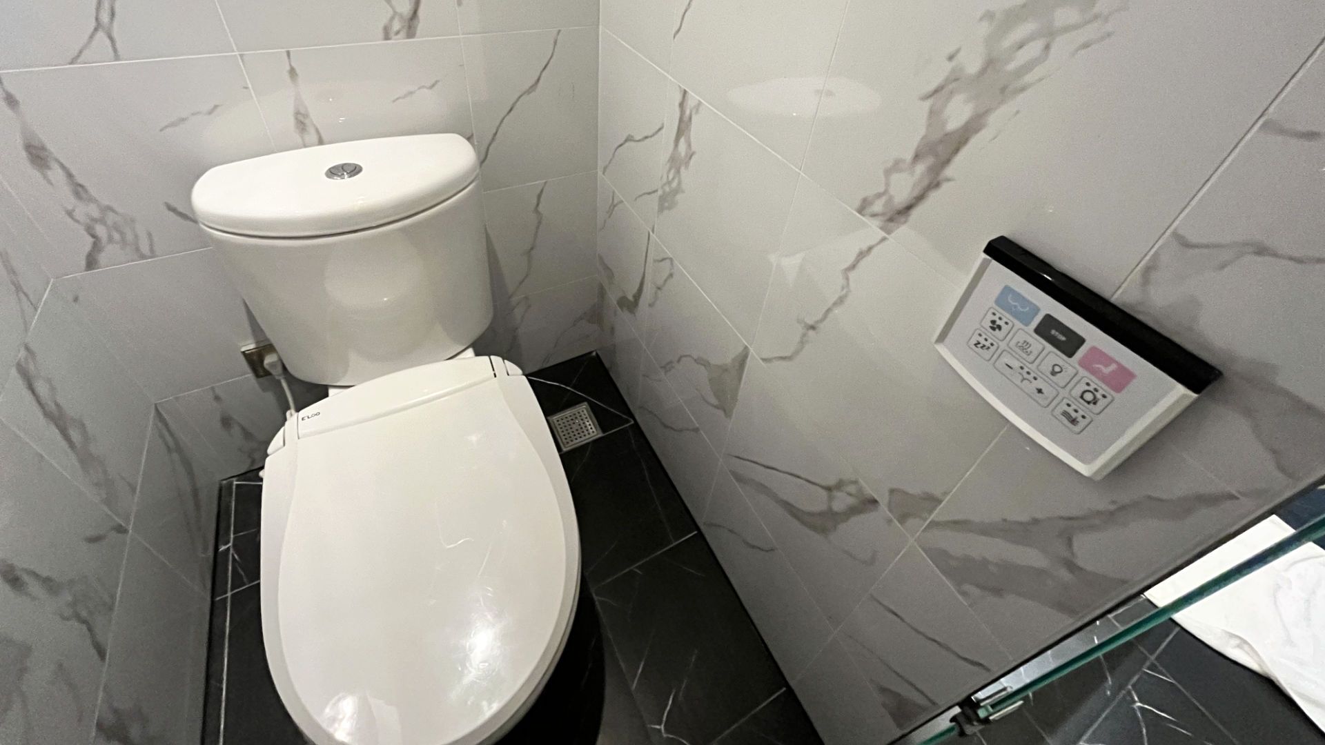 A toilet next to a wall-mounted remote control panel.