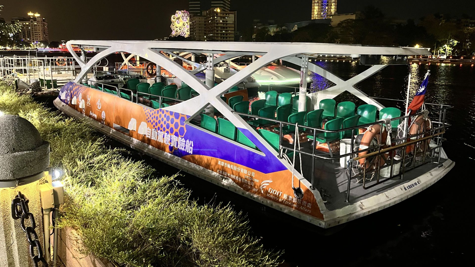 An electric tour boat docked at the side of Love River. It looks to have perhaps 30 or 40 seats.