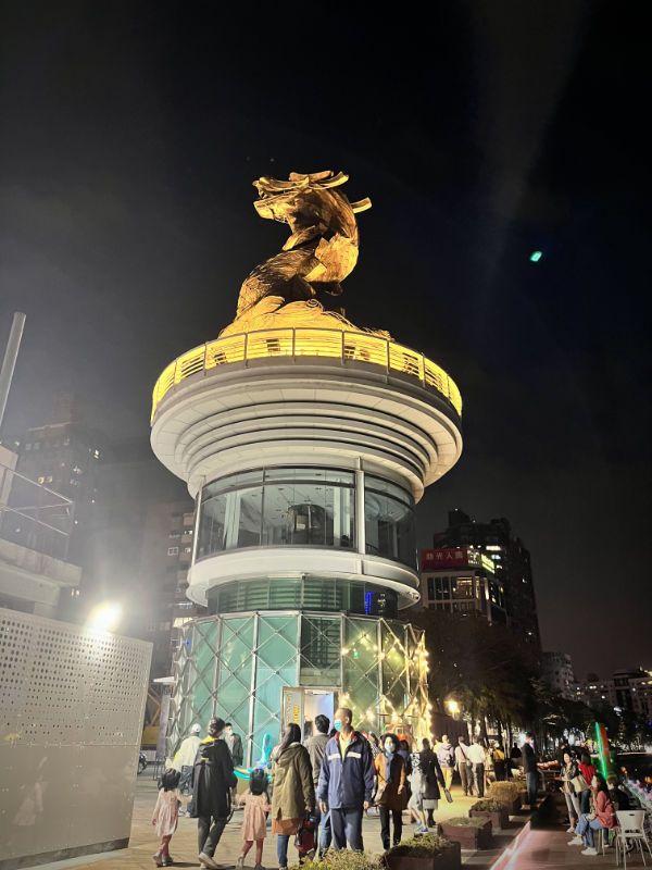 A round glass platform, approximately two stories high, with a large golden dragonhead sculpture on top, facing away from the river.