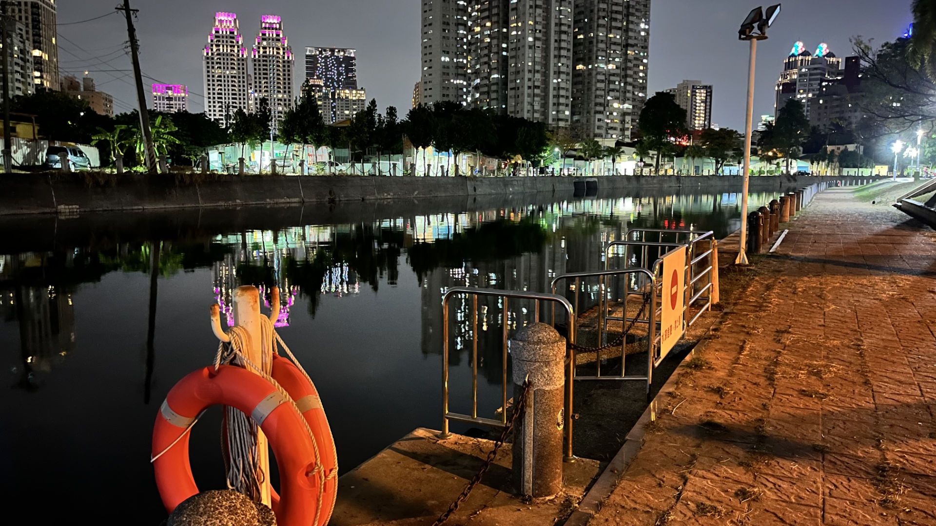 Two lifebuoys hanging next to the river. The water is still, reflecting tall buildings.