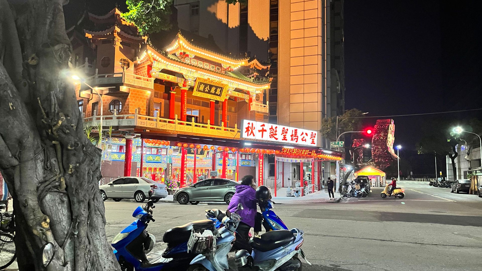 An urban intersection with a red and gold temple on one corner.