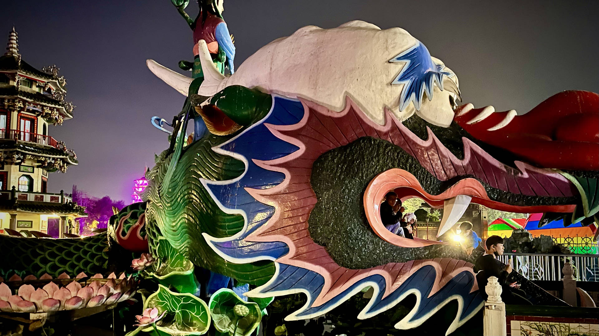 Two people sitting in the mouth of a dragon statue.