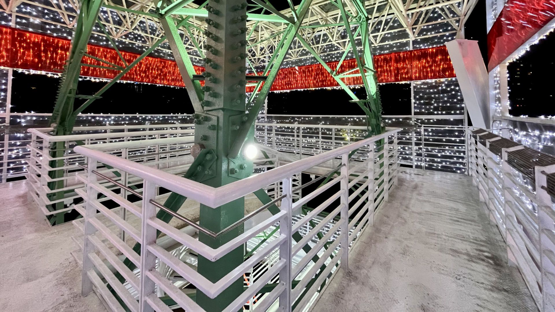 A square viewing platform wrapped around the pylon and brightly illuminated with red and white lights.