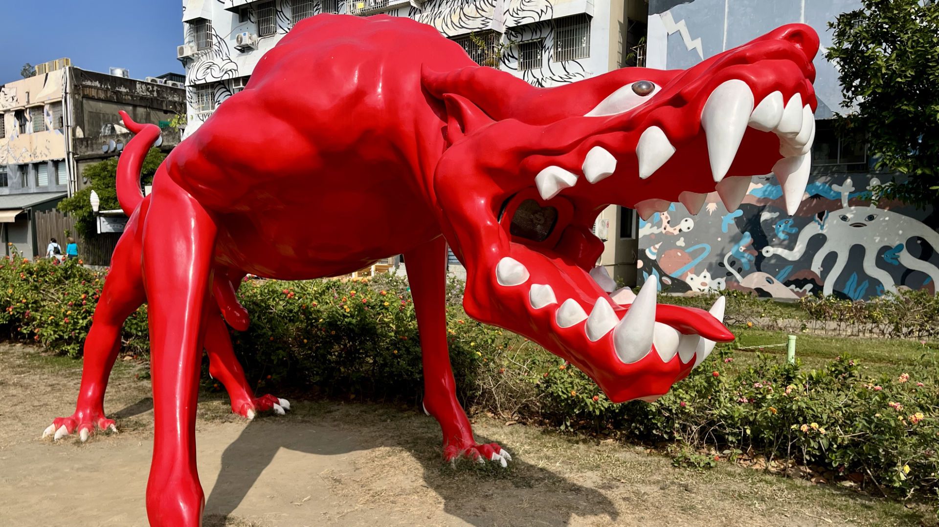 A sculpture of a large, bright red, dog-like creature with fierce teeth and eyes.