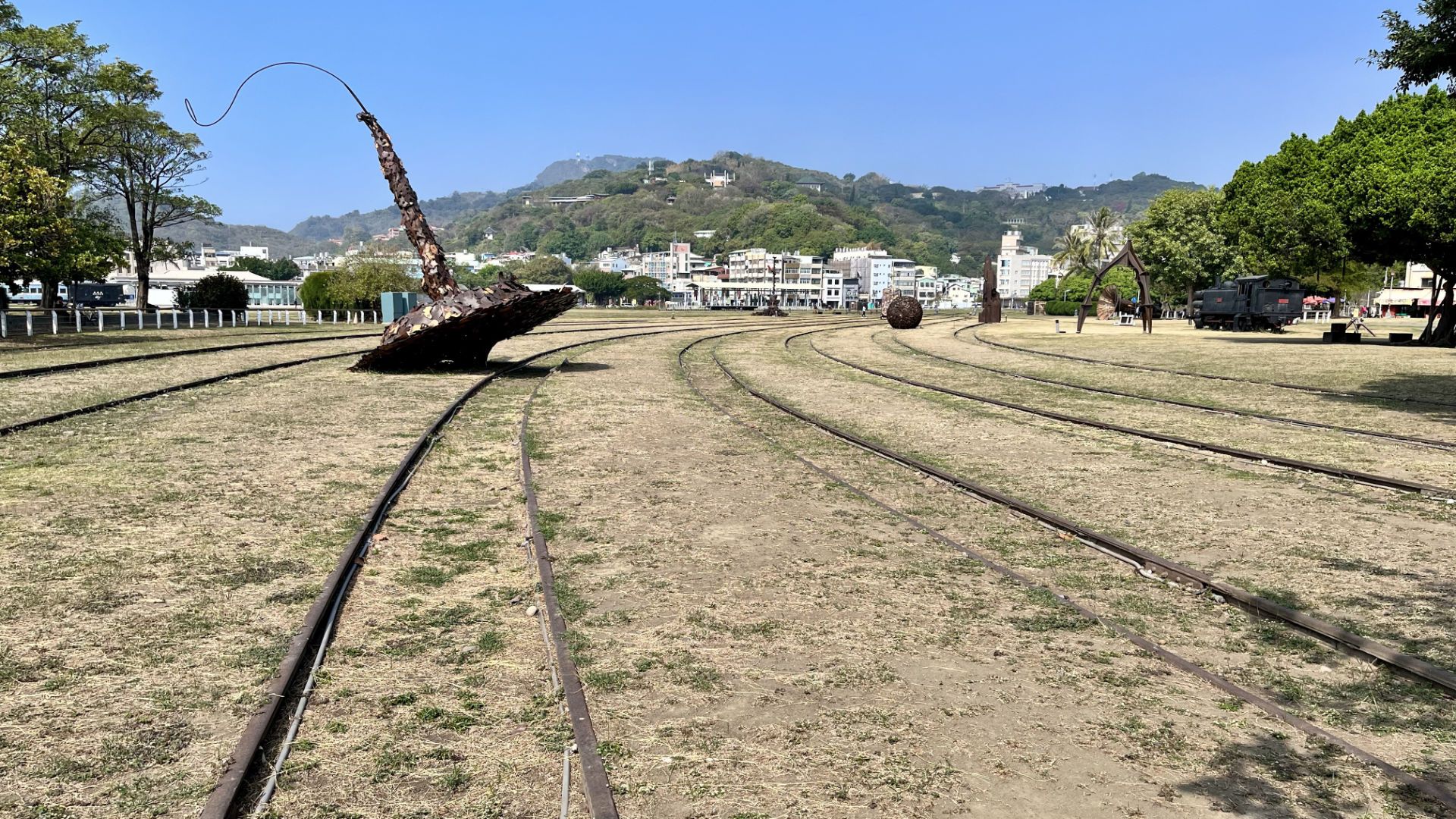 A metal sculpture of a giant spinning top, approximately 5 meters tall, resting on disused railway tracks.