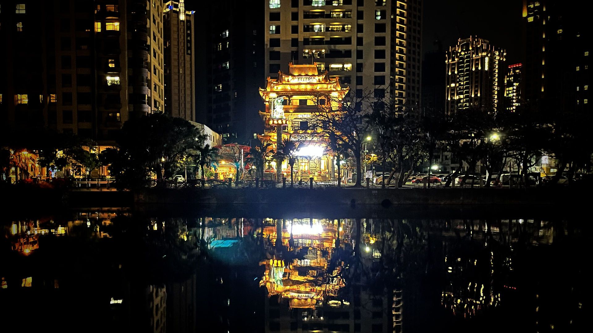 A golden temple on the other side of the river, with tall buildings behind it.