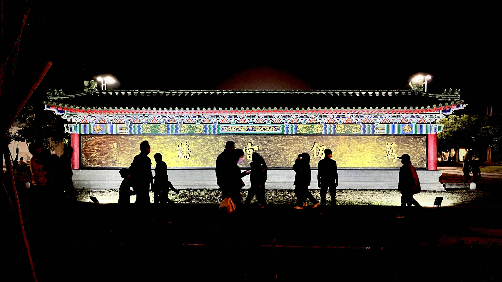  Pedestrians silhouetted against a colorful temple wall.