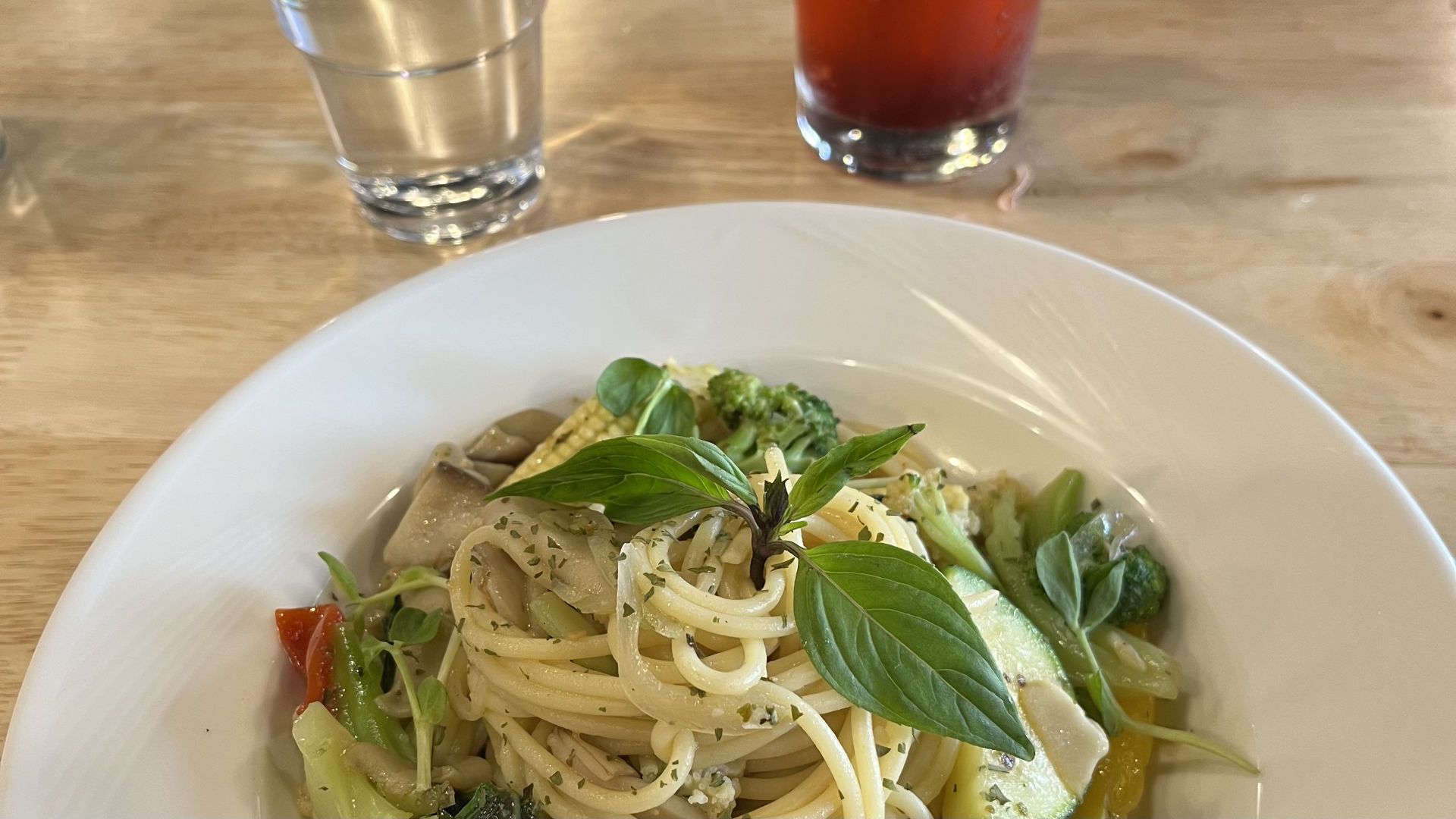 Close-up of a vegetable pasta dish with a glass of strawberry juice and a glass of water in the background.