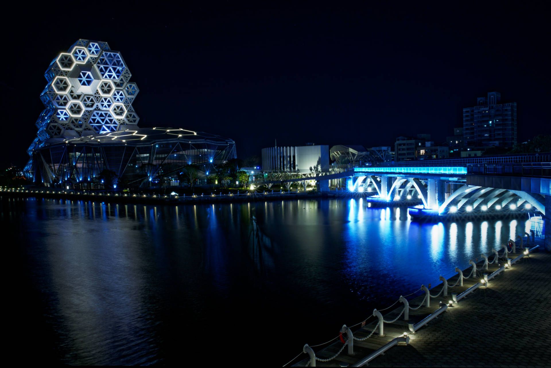 Night-time shot of the mouth of Love River, Kaohsiung, with buildings and bridges illuminated in turquoise.