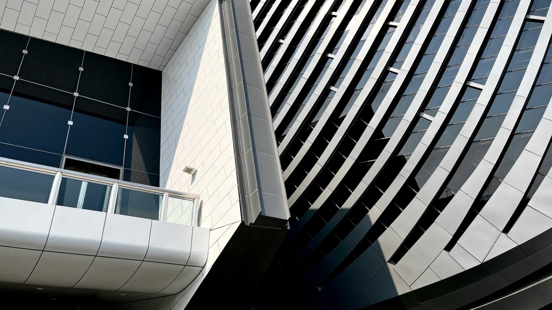 Closer view of a cantilevered balcony with a curved metallic and glass wall beside it.