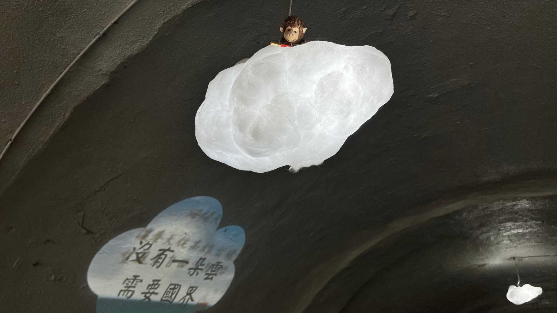 A sculpture of a monkey riding a cloud hangs from the ceiling. A cloud-shaped video of Chinese characters is projected on the tunnel wall.