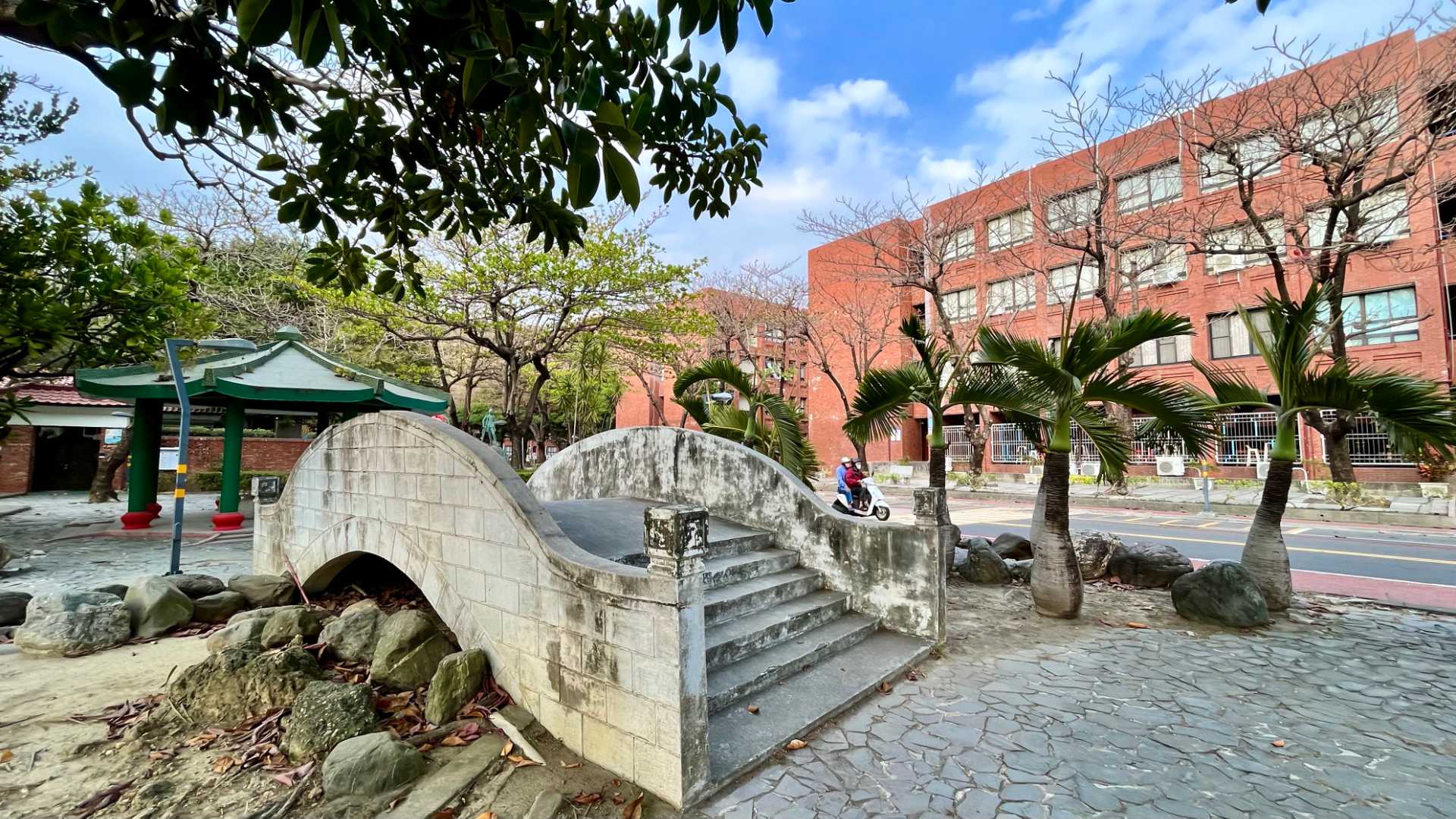 A small concrete bridge in the foreground with a pagoda and multi-story university buildings behind.