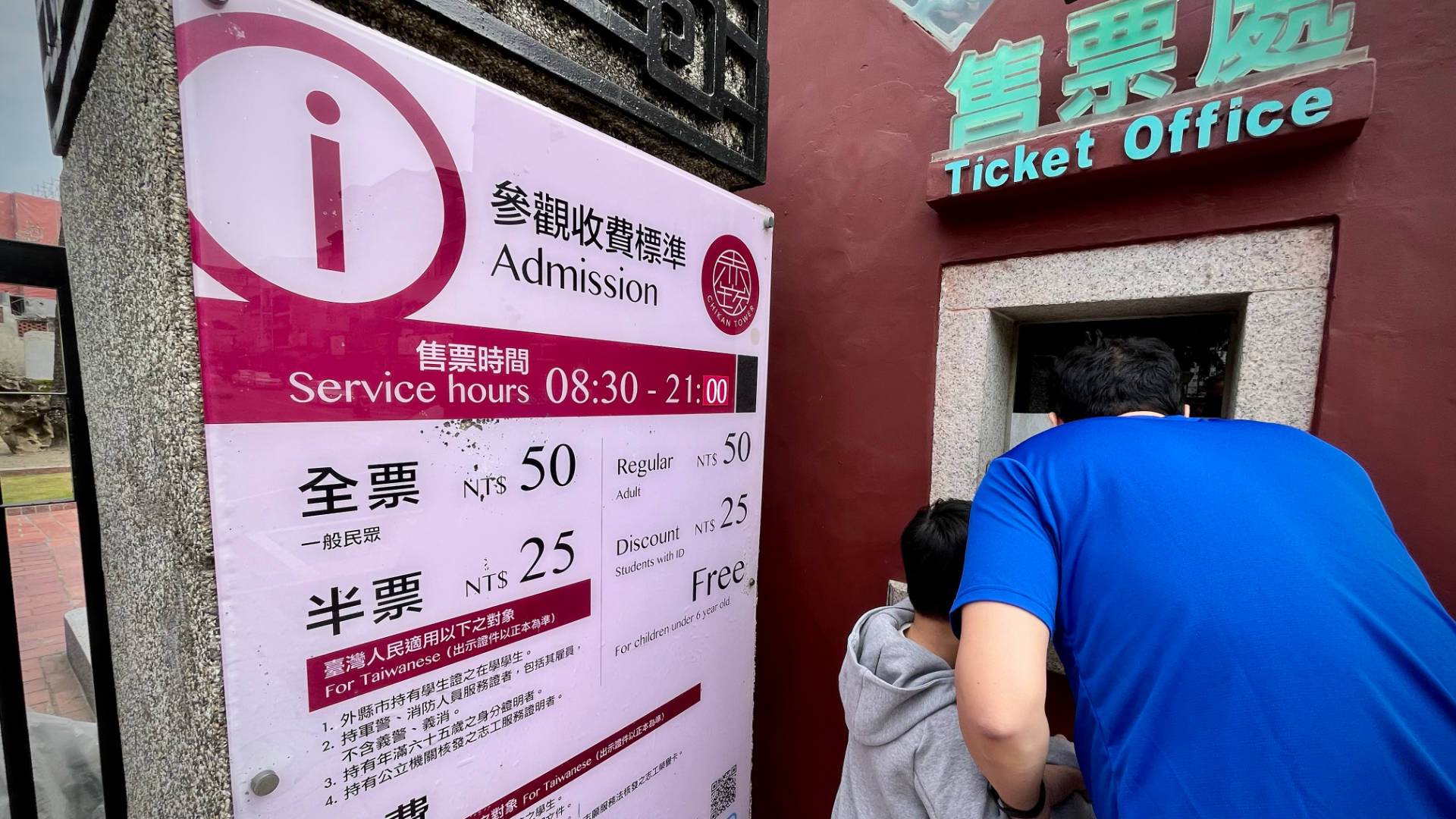 An adult and child buying tickets from a small window. Signage is in Chinese.