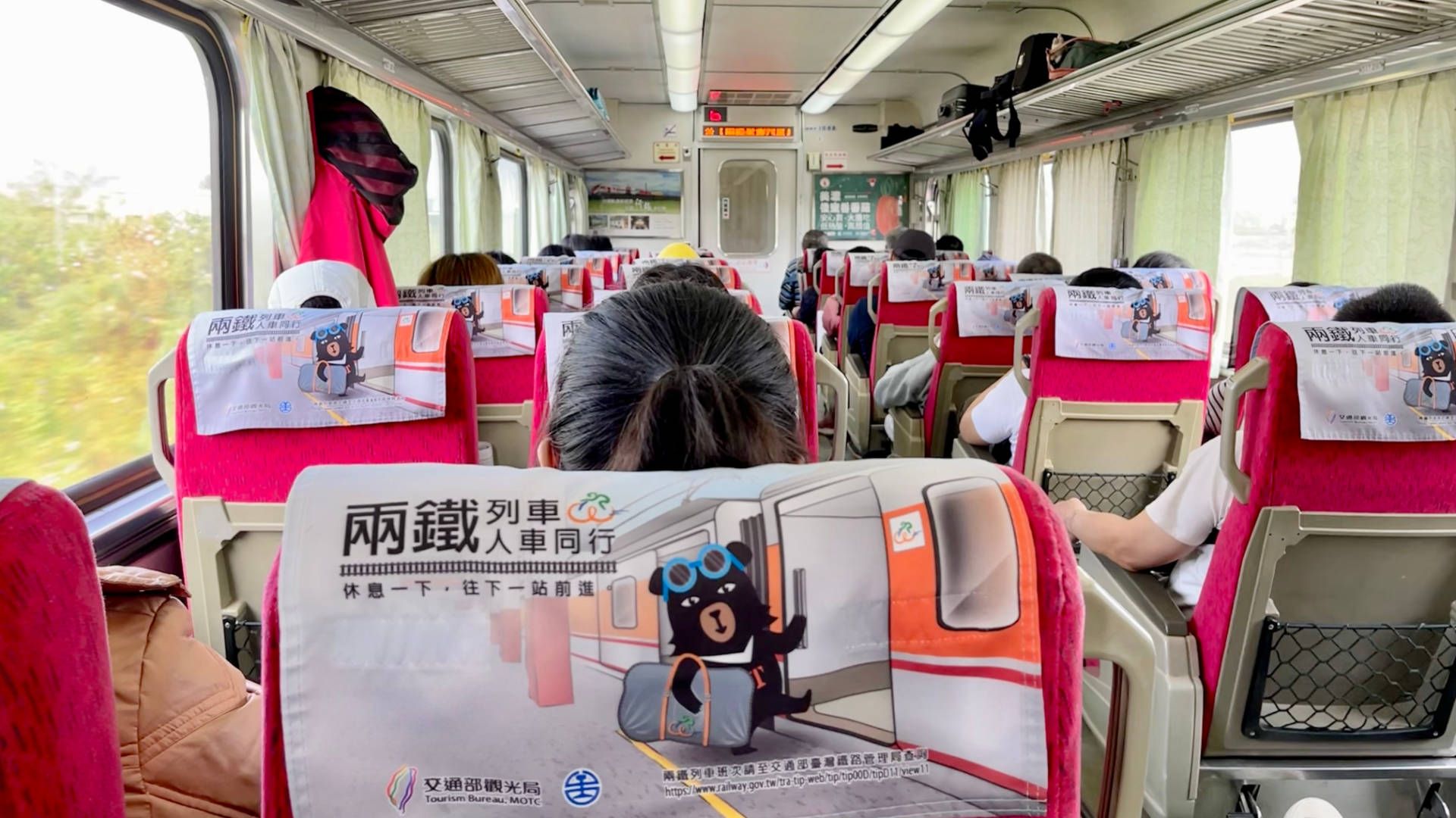 Interior of a train carriage. All seats appear to be taken. There are four seats in each row; two either side of the aisle.