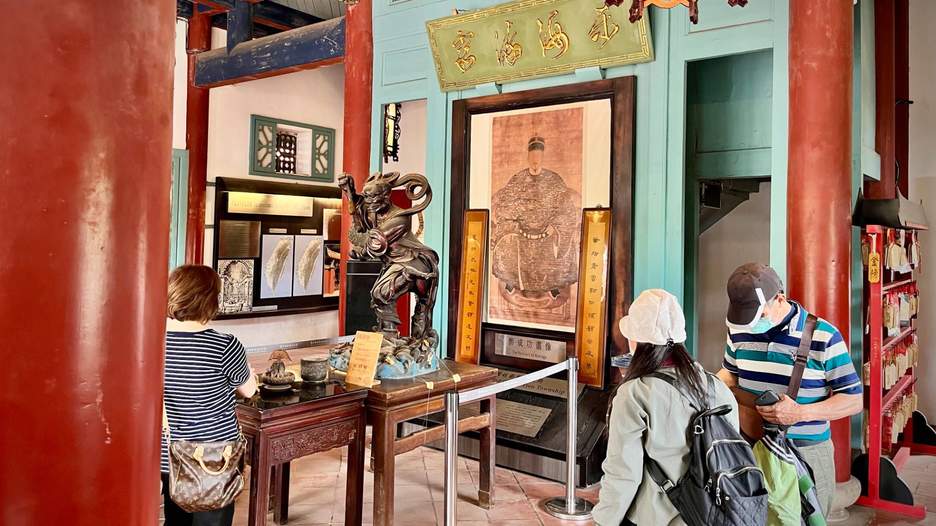 Inside the ground floor of Chihkan Tower. A statue of a god is at center, with tourists standing around. A rack of wooden handing cards is on the right.