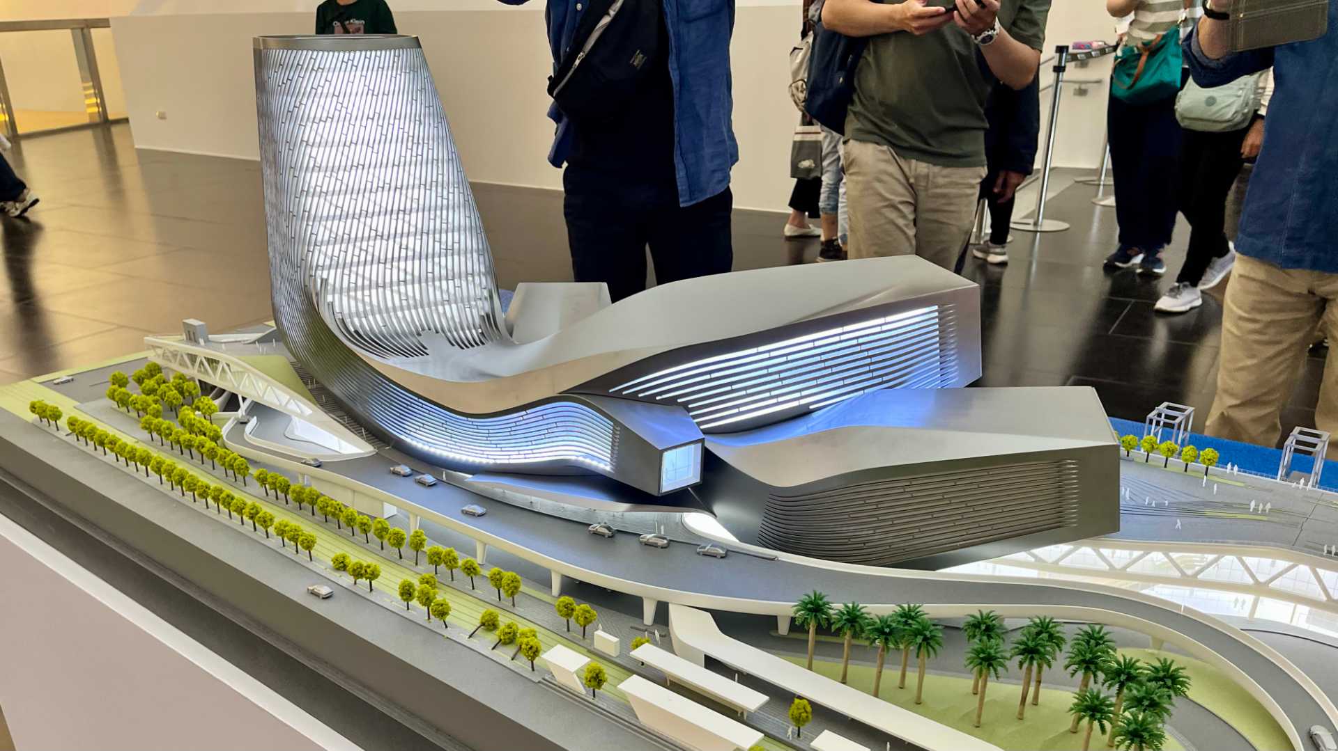 A 3D model of the Kaohsiung Port Cruise Terminal, with illuminated windows. The model is approximately 1 meter high, with people standing around taking photos of it.