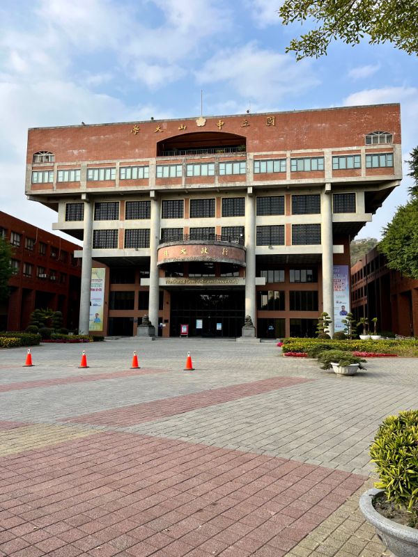 A 7-story building made of red brick and unpainted concrete. The building shape is inverted—with the floors getting wider towards the top.