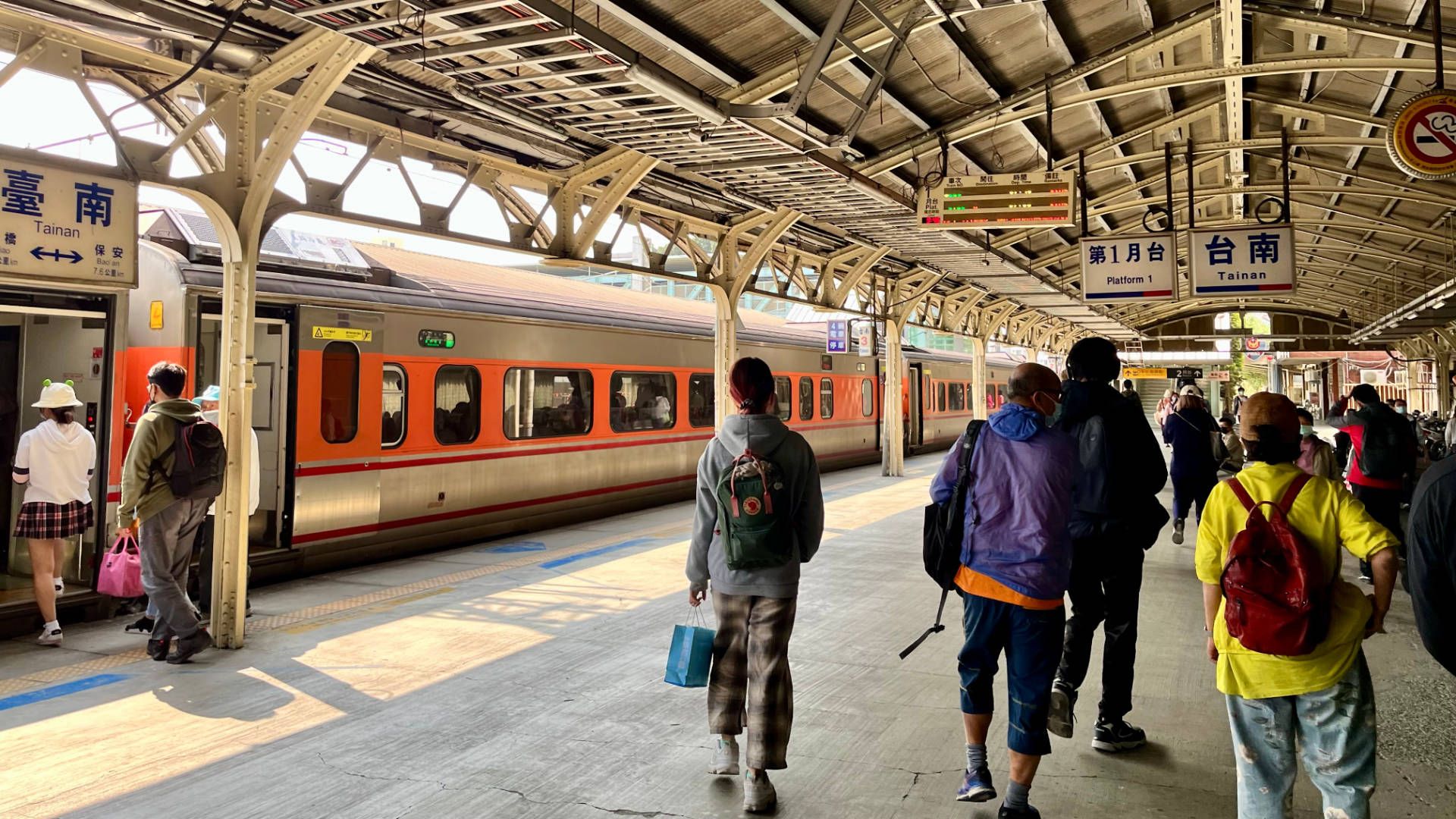 People standing on an outdoor platform at Tainan Station. The train is visible to the left. The platform has a older-style wrought-iron roof structure.