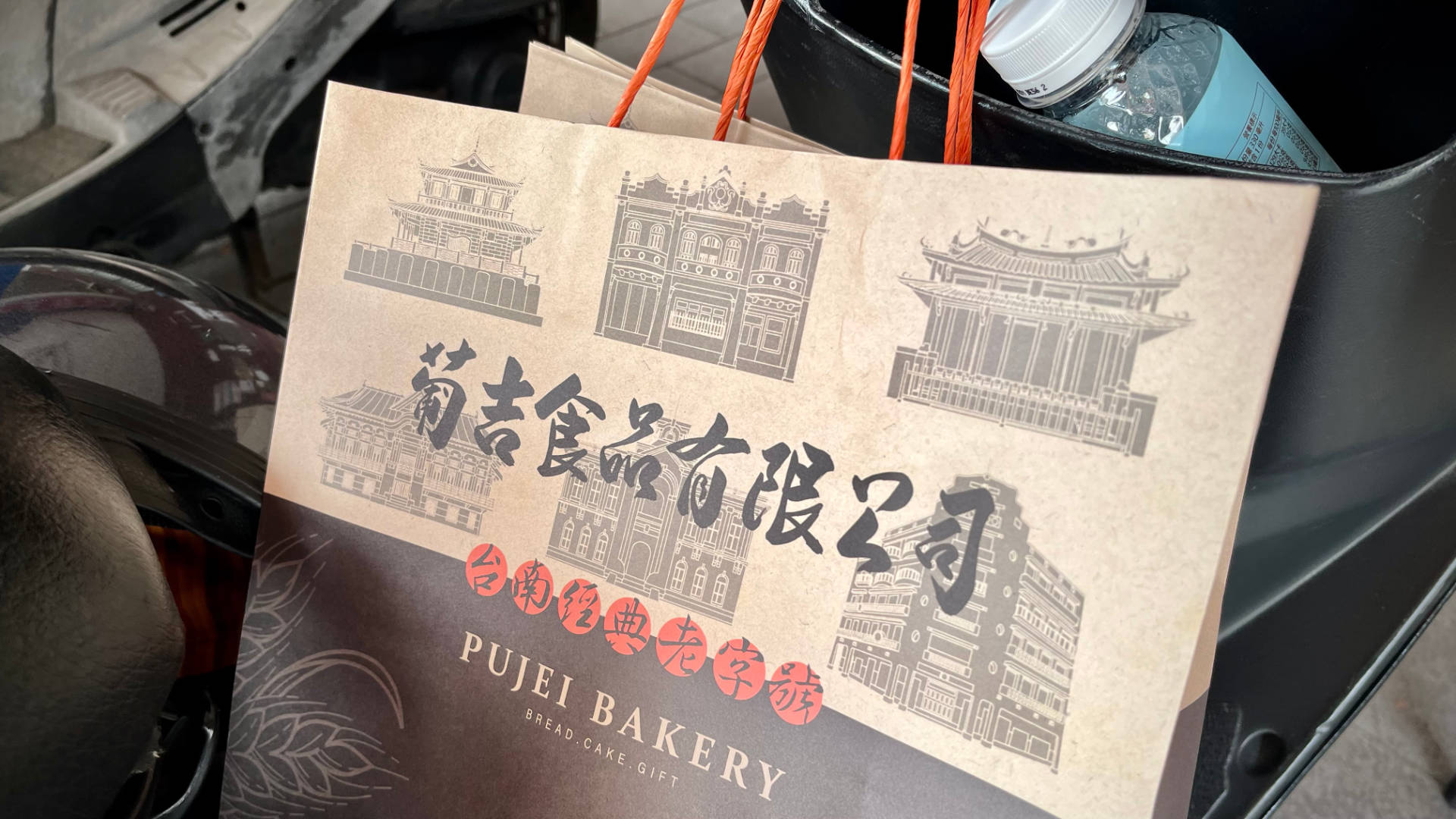 A Pujei Bakery paper shopping bag, hanging on a scooter.