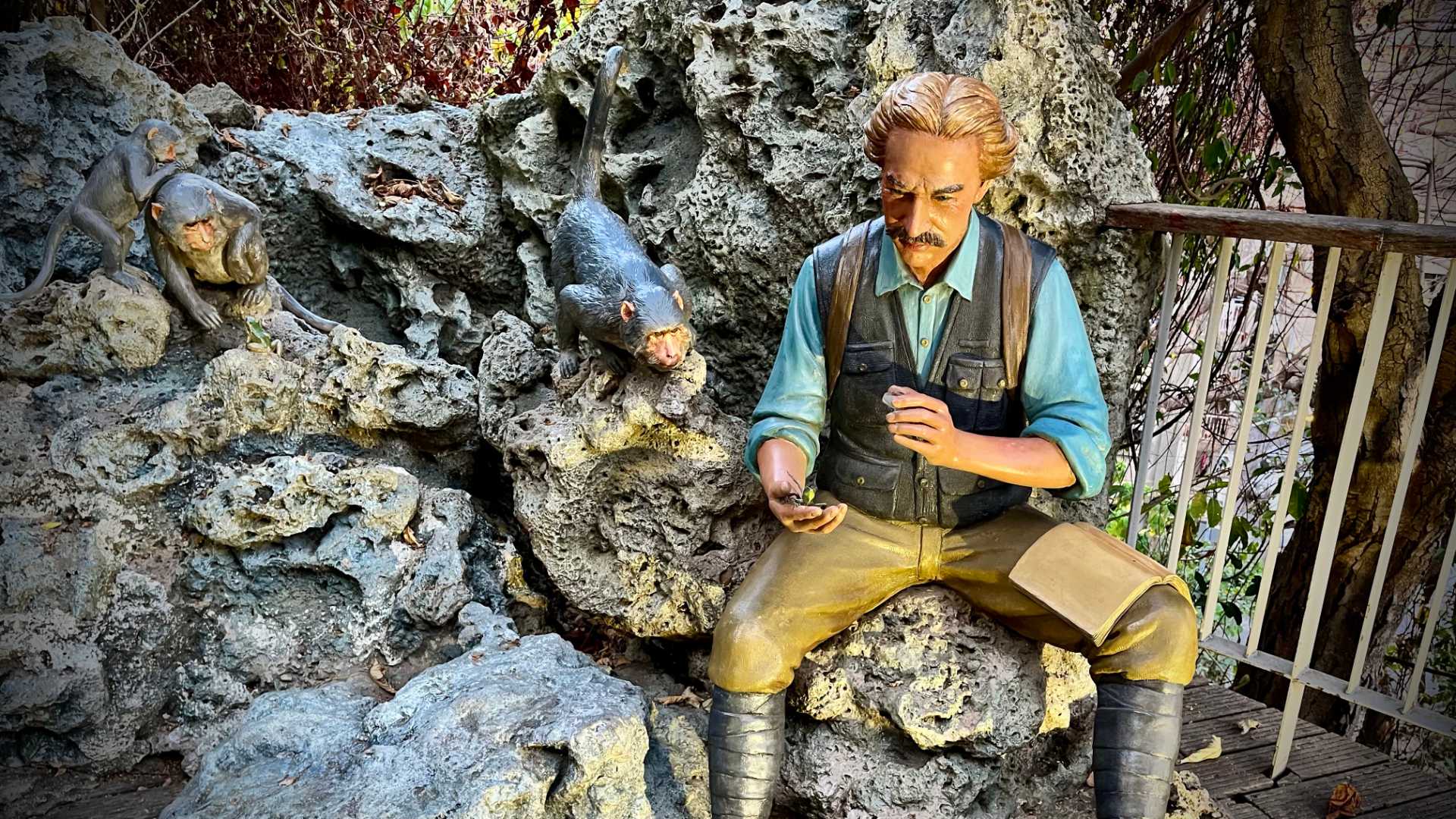 Life-size statue of Robert Swinhoe sitting on limestone rocks, with three monkeys alongside him watching.