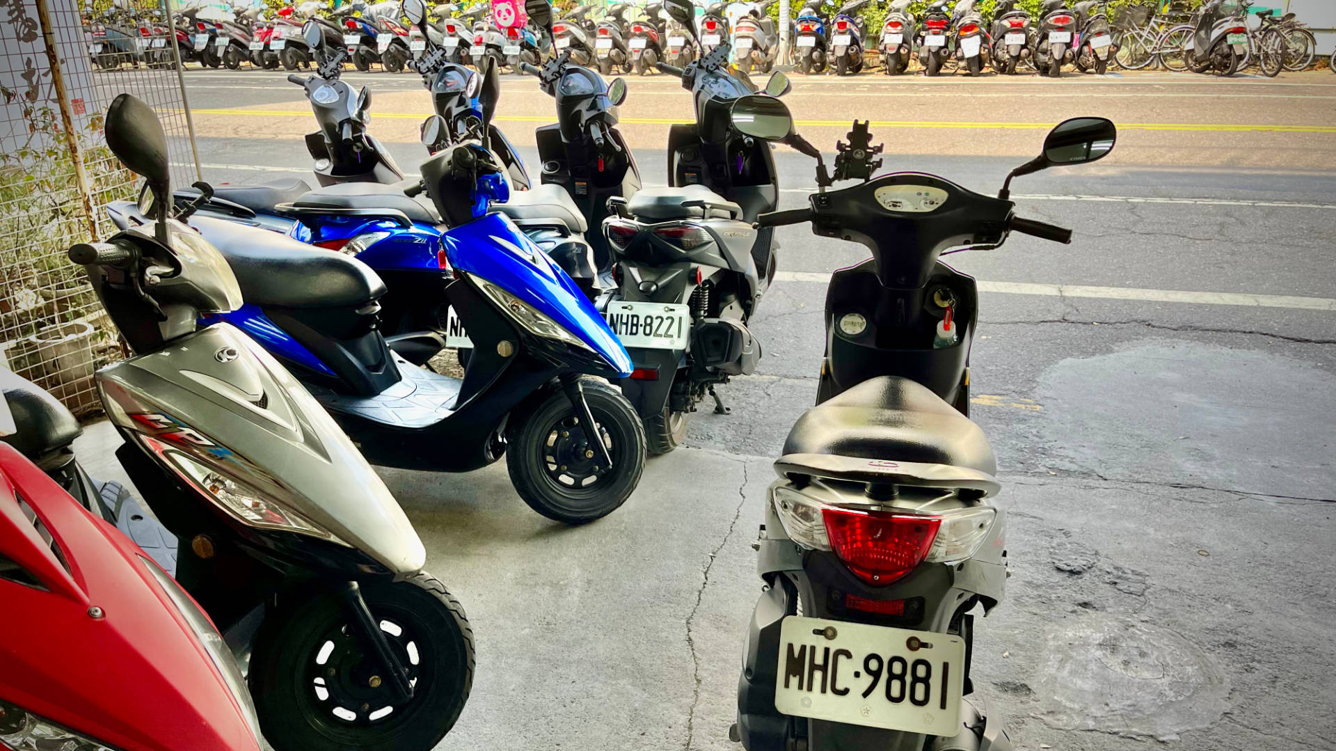 A motorbike with the licence plate MHC9881 in the foreground, with dozens of other scooters parked either side of the road.