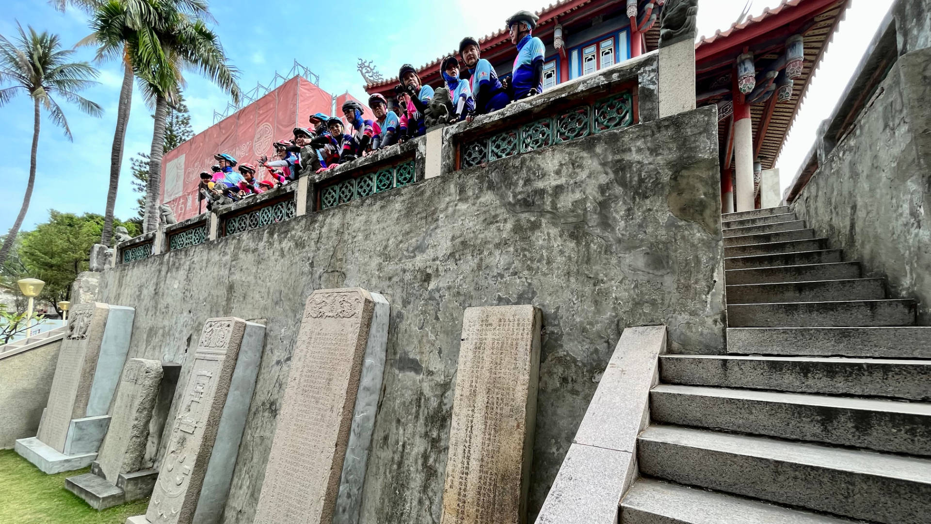 A group of approximately 20 cyclists looking at the view from the balcony, above some stone tablets and a stone staircase.