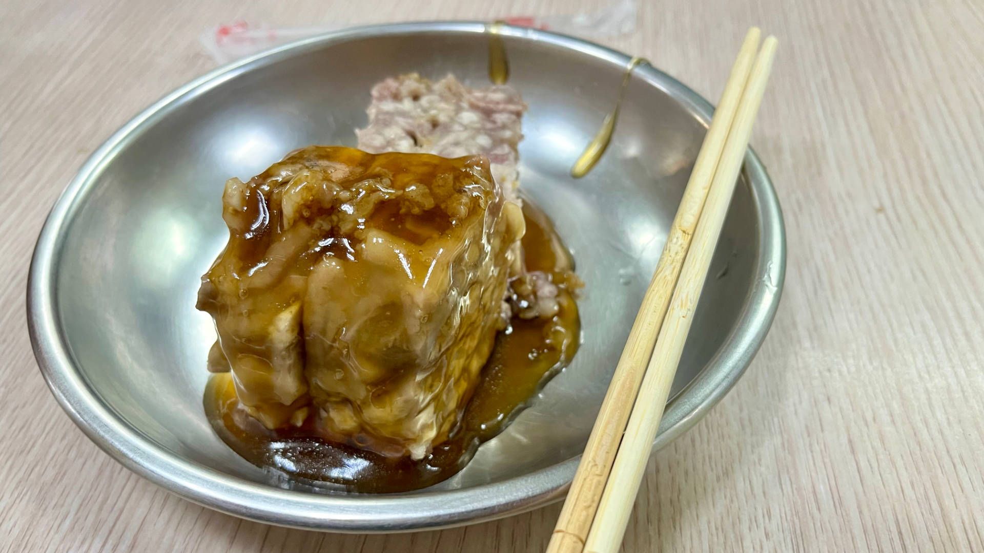 A steel bowl of taro glutinous rice smothered in a rich brown sauce, with wooden chopsticks resting on the bowl.
