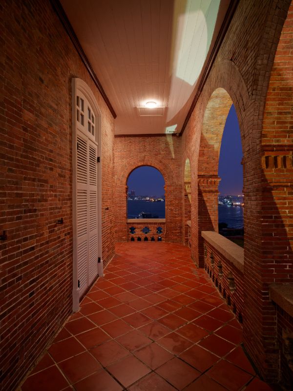 The verandah with harbor and city views in the distance, through the verandah’s red brick arches.