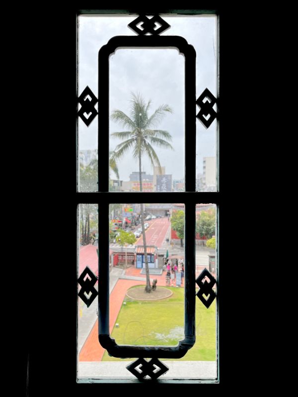 View of the park-like grounds around Chihkan Tower, through a silhouetted wooden window frame.