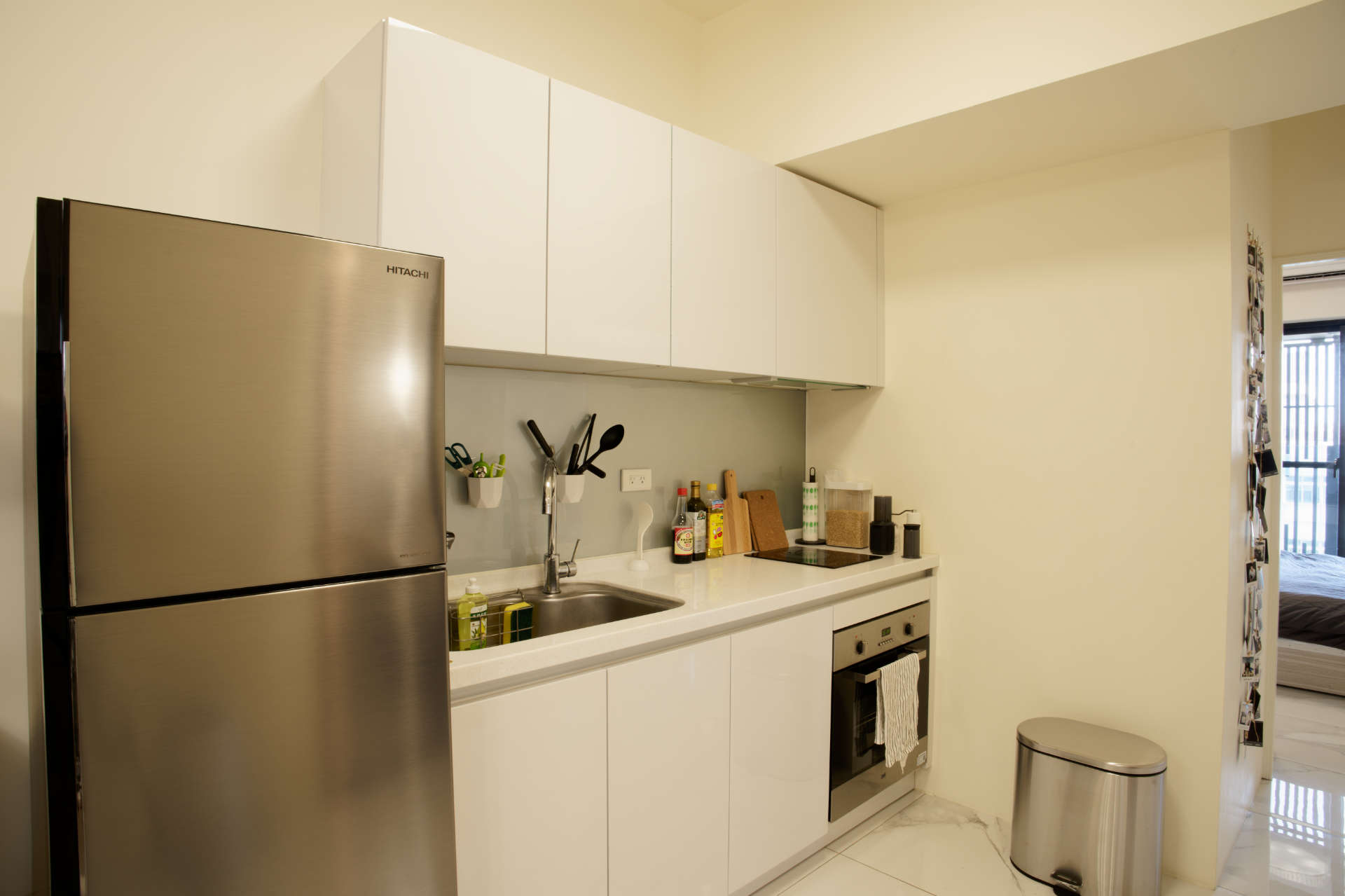 A kitchen with sink, induction cooktop, oven, fridge, and stainless steel trash bin.