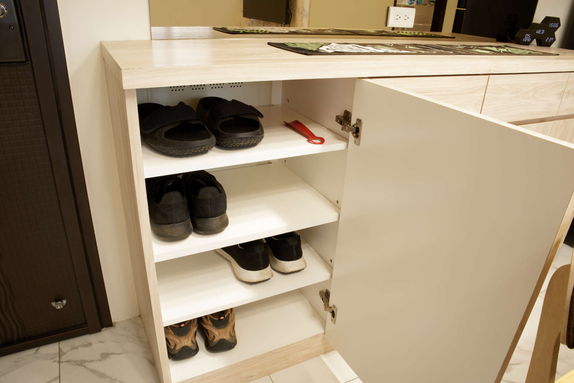 An open shoe cupboard, with shoes on four shelves. A metal grate can be seen on the back wall of the cupboard.
