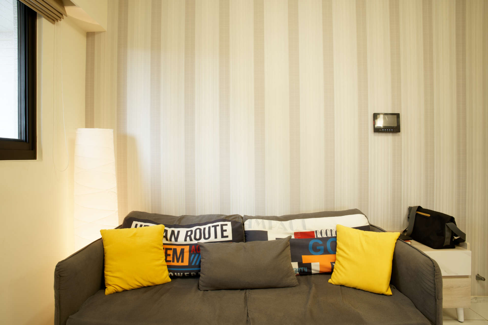 A couch with various phrases printed on the cushions, and a paper floor lamp beside it.