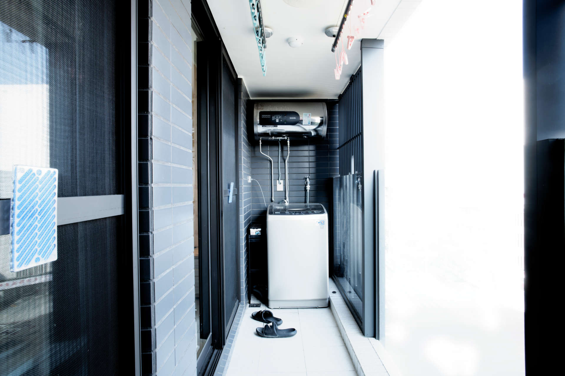 A washing machine on a balcony, with hot water heater and clothes lines mounted above.