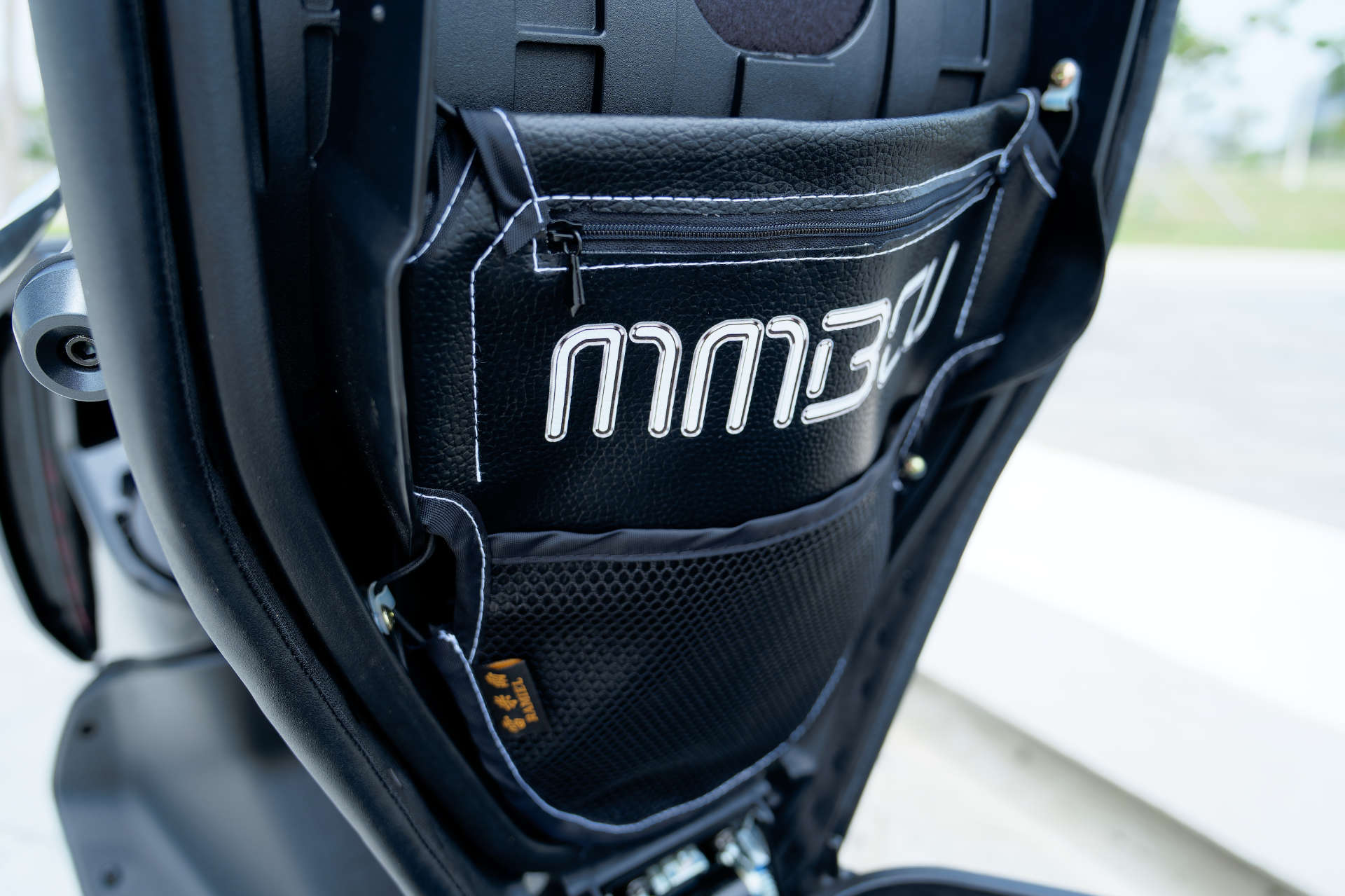 An MMBCU-branded under-seat storage pocket mounted to the underside of an SYM MMBCU scooter seat.