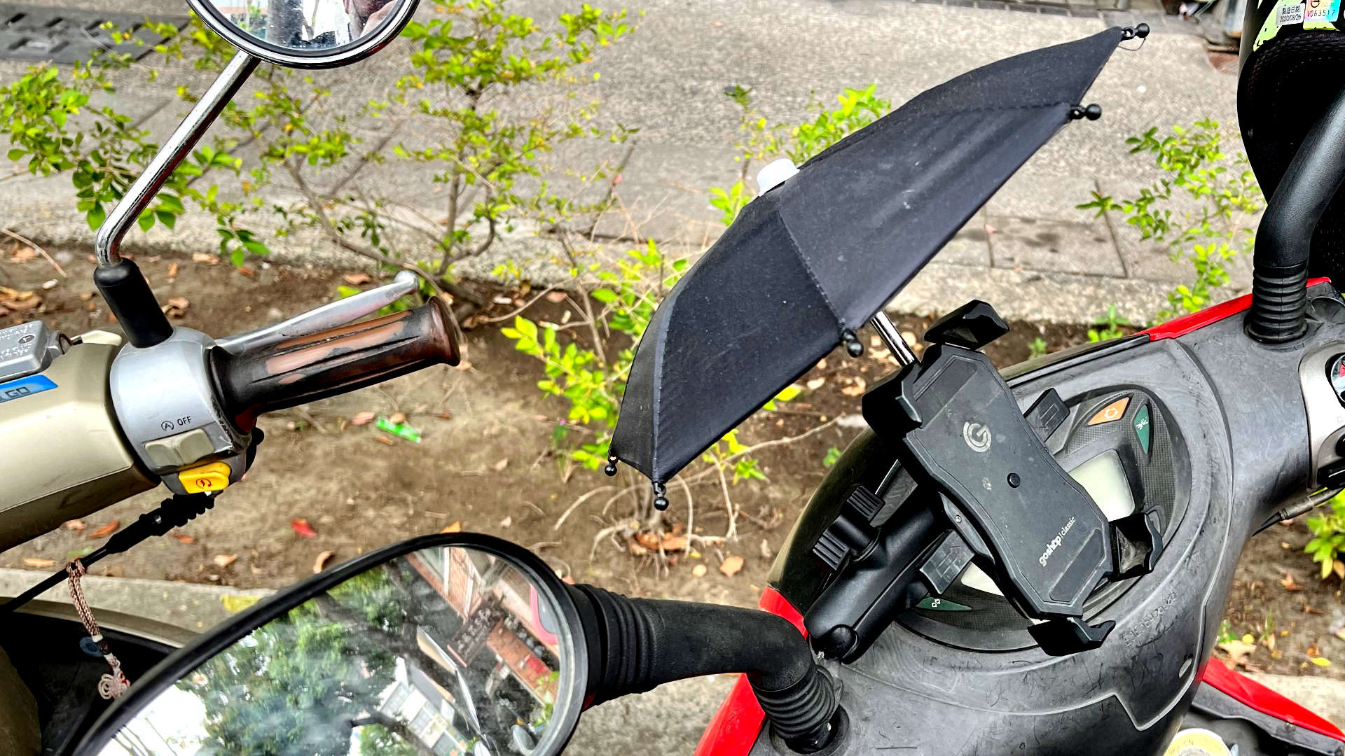 Mobile phone umbrella affixed to a scooter.