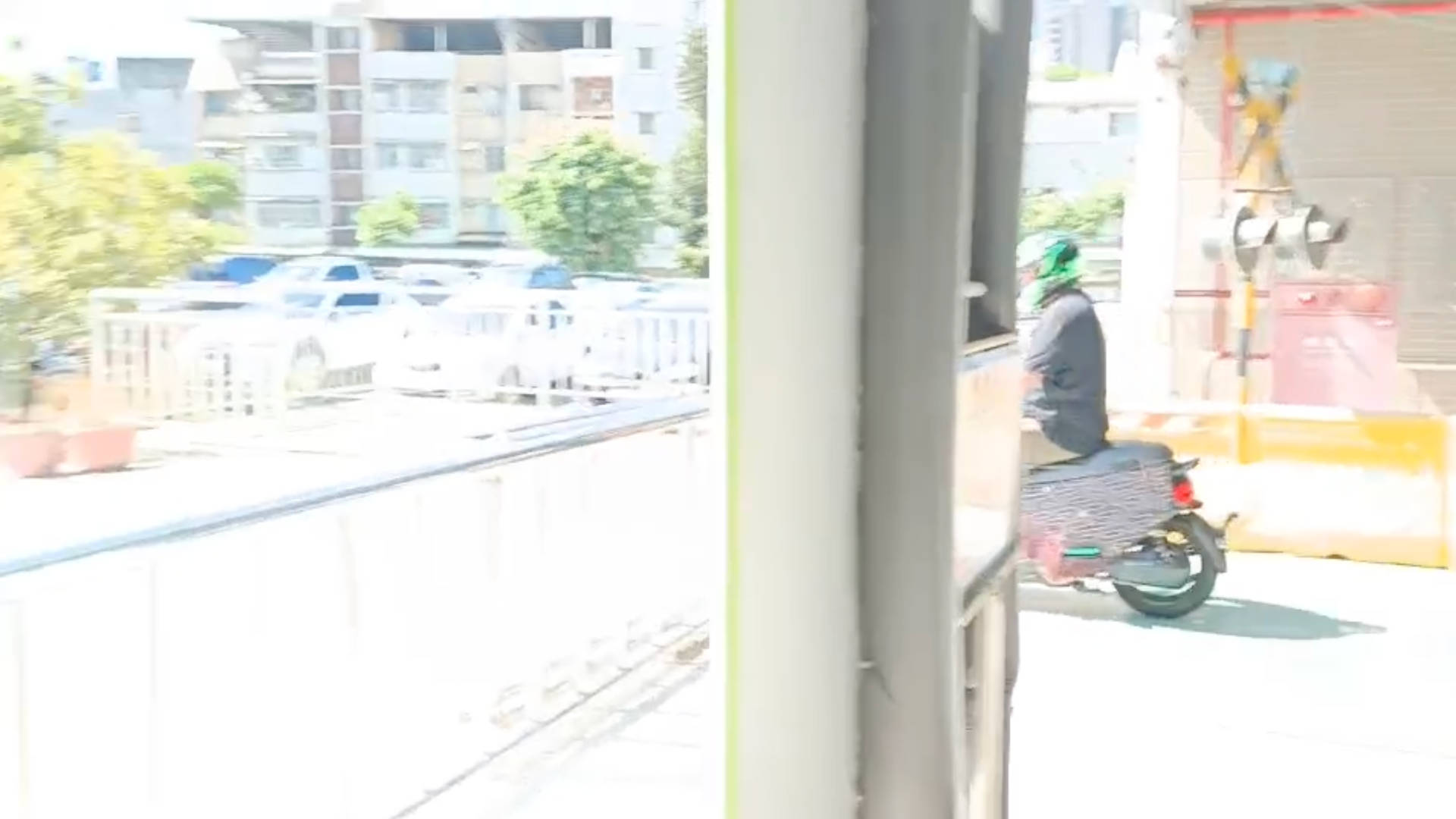 A scooter rider passes the finish line of the Taiwan scooter driving test. A railway crossing sign and lights are visible in the background.