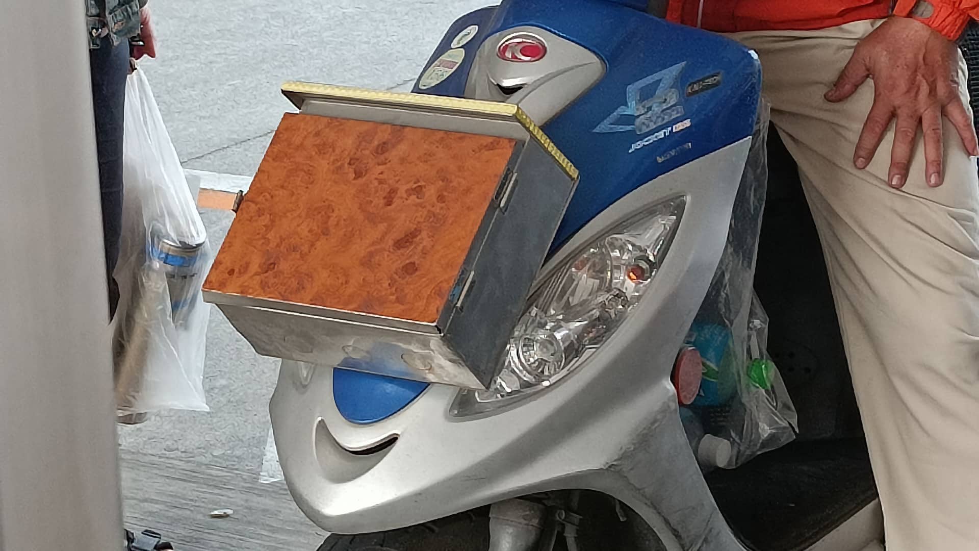 A metal mailbox mounted to the front of a Kymco scooter.