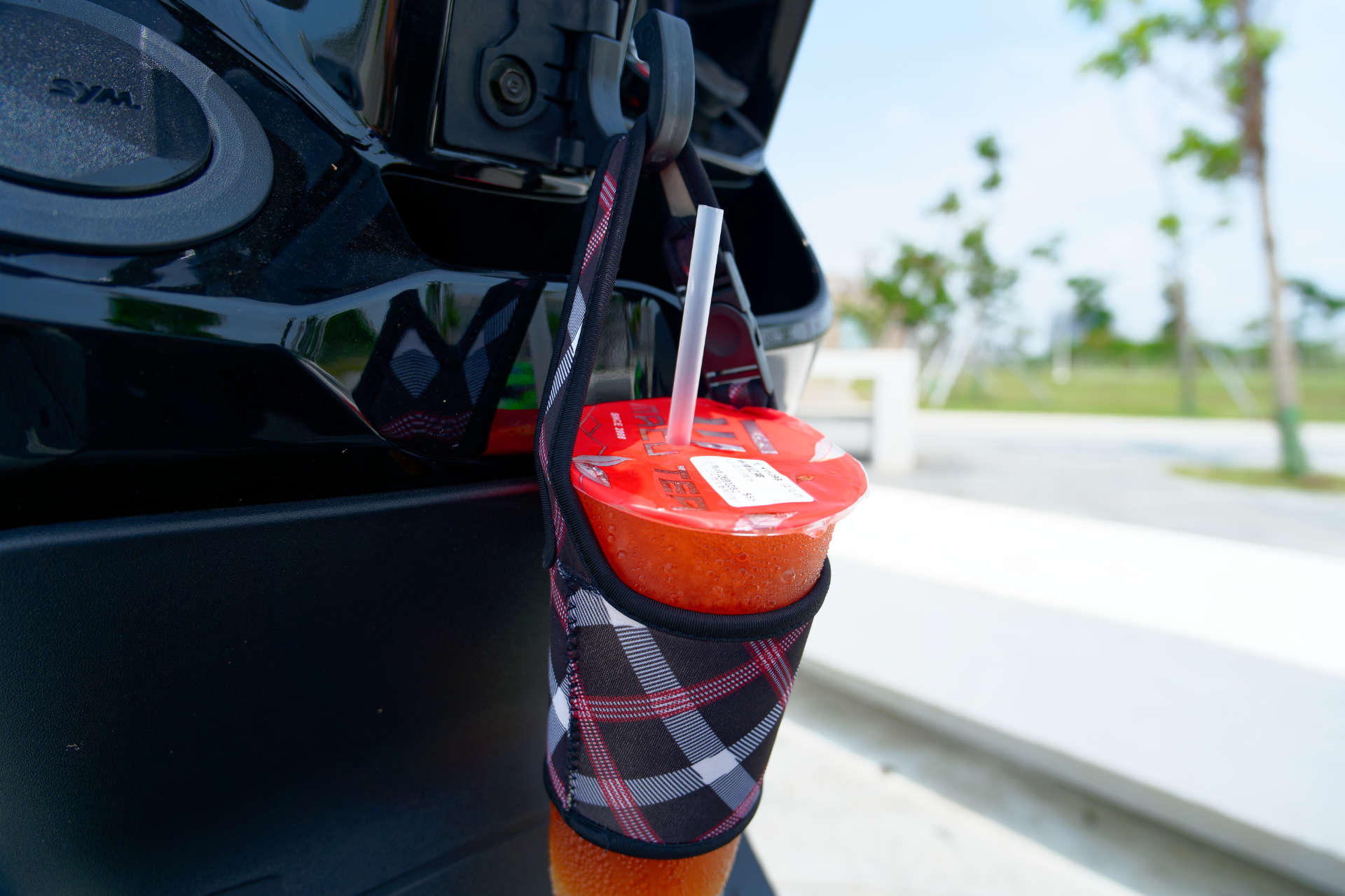 A cup of sugar-free iced lemon black tea in a tea holder, hanging from a hook on an SYM scooter.