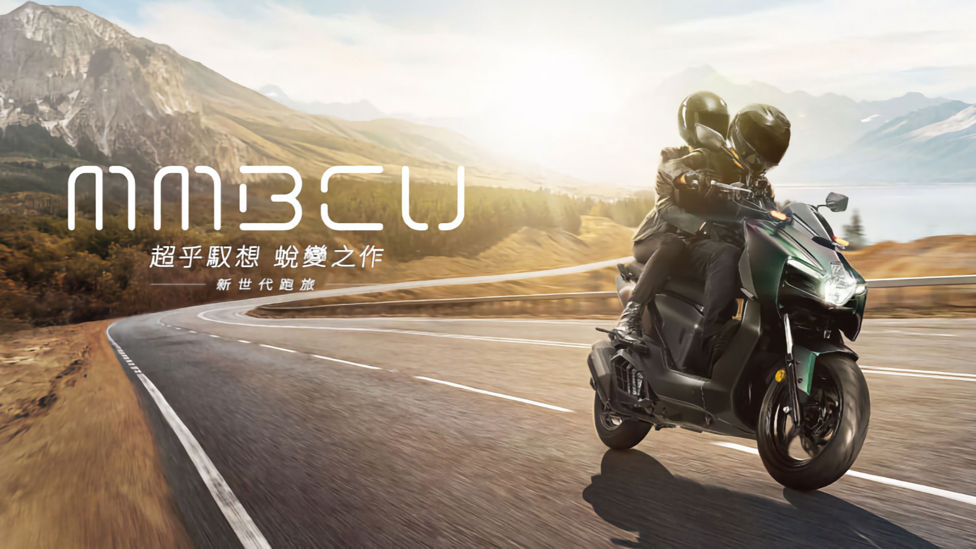 Marketing image of two people riding an SYM MMBCU scooter on a mountain highway.