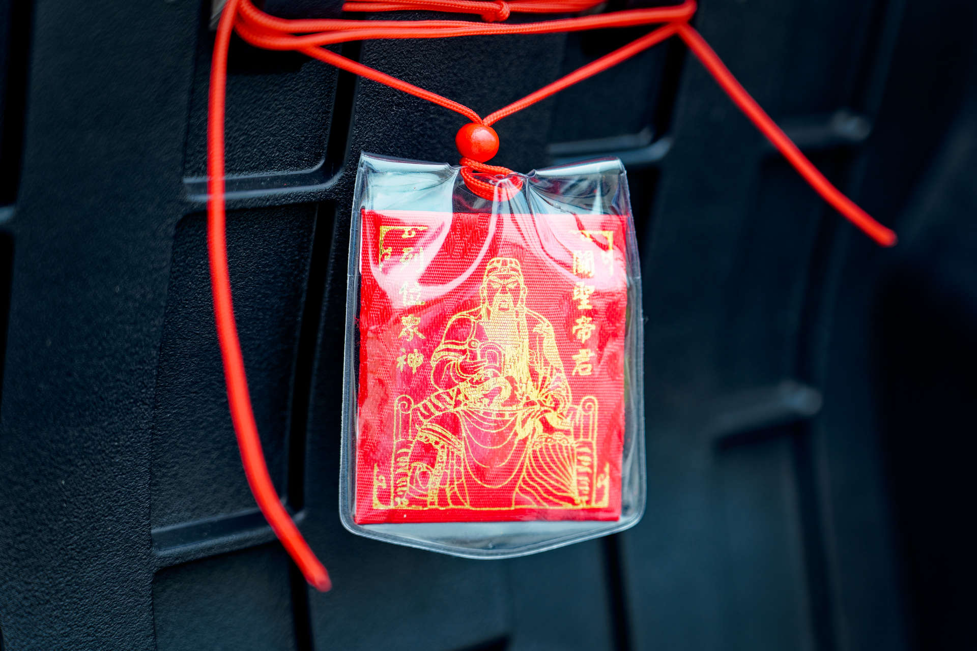 A red and gold Taoist good luck charm, hanging from the underside of a scooter seat.