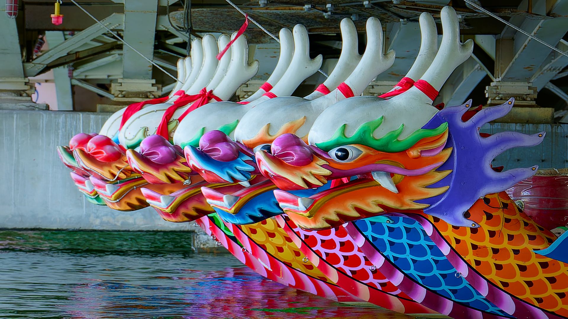 Approximately 10 large dragon boats moored under a bridge.