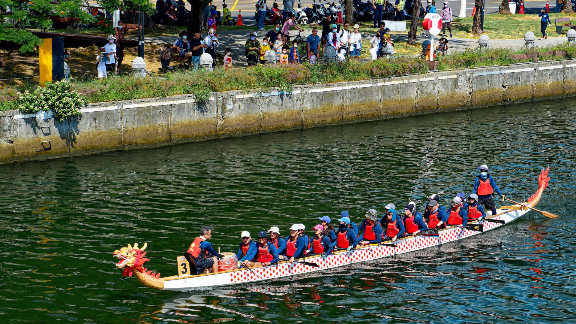 A relaxed dragon boat crew paddling past spectators after a race.