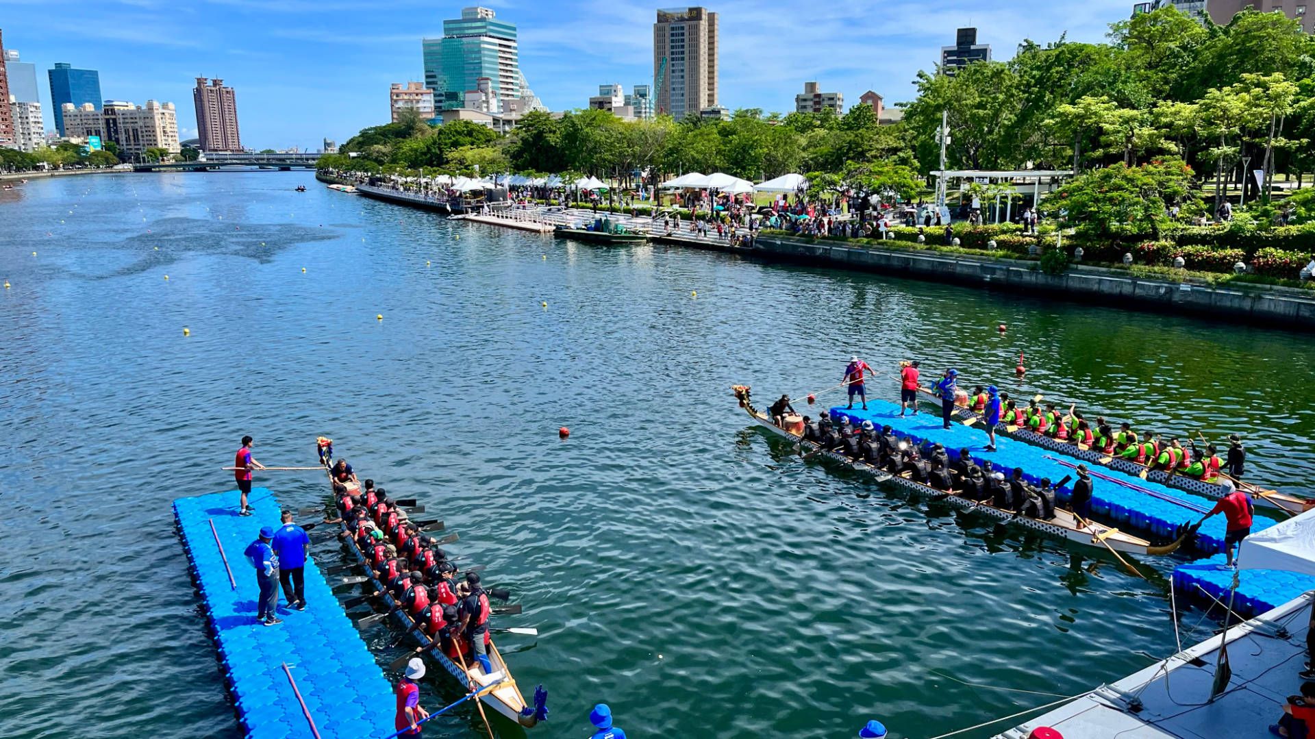 Three dragon boats at the starting gate on Love River, Kaohsiung. It is a beautiful sunny day with calm water and a blue sky.