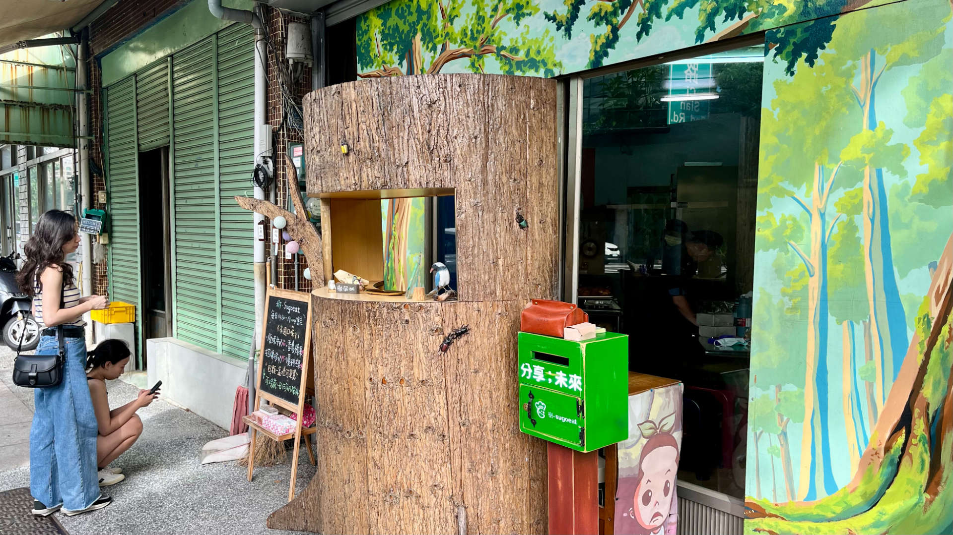 A large synthetic tree trunk on a footpath, with a window cut in the front—though which the staff can serve customers.