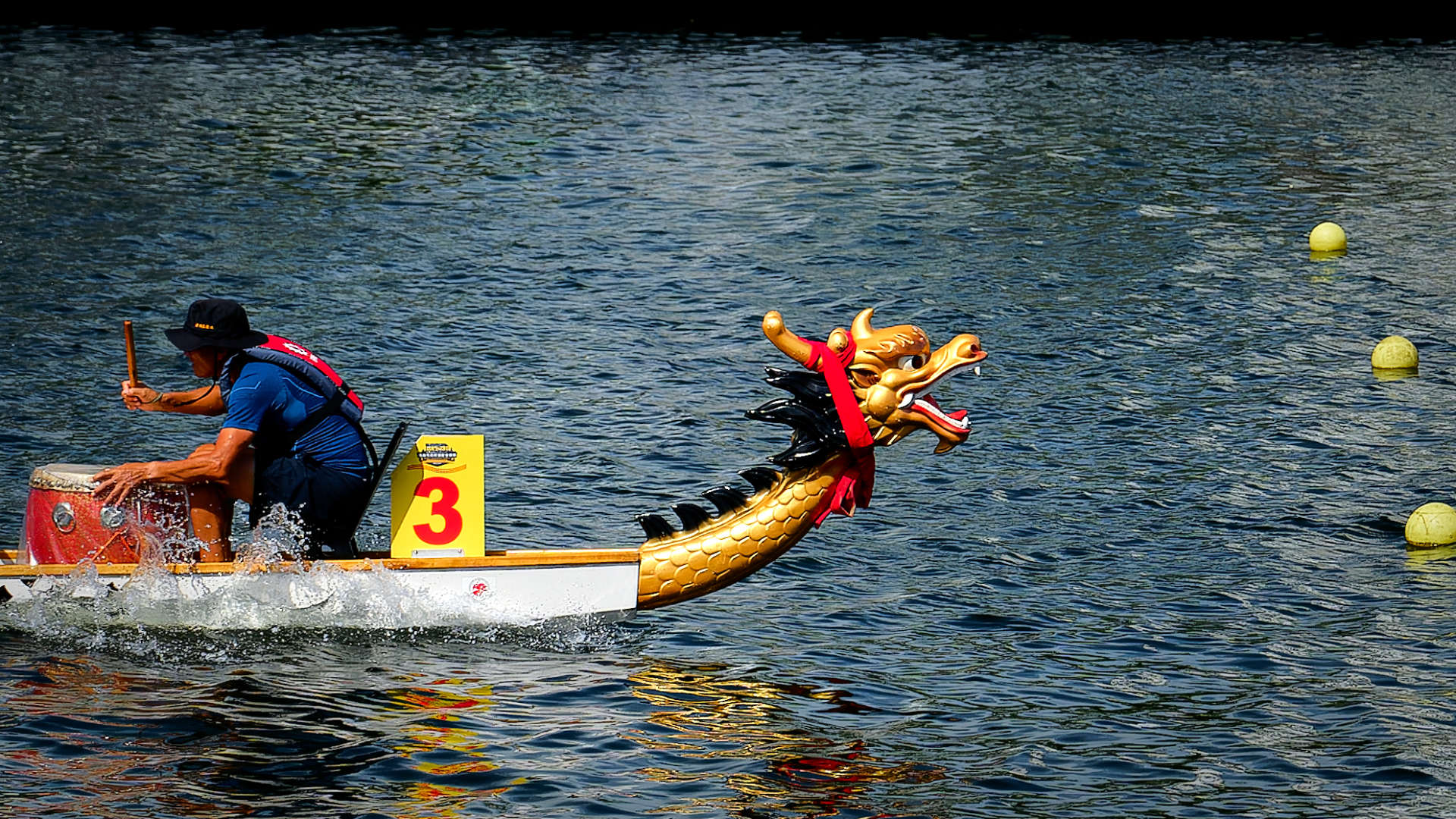 The front of a Taiwanese dragon boat, showing a decorative dragon head and a crew member beating a drum.