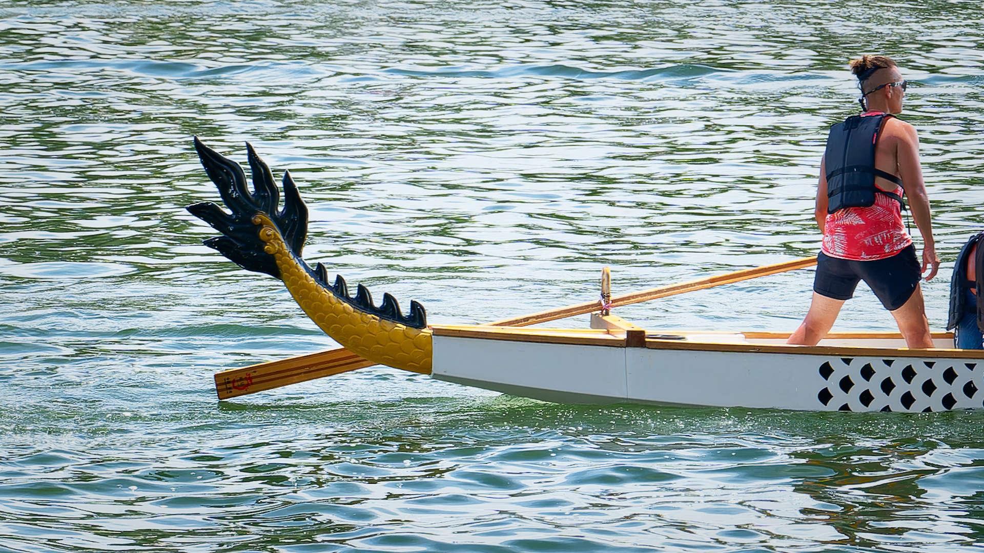A steerer standing near the back of a dragon boat. The very end of the boat is decorated with a dragon tail.